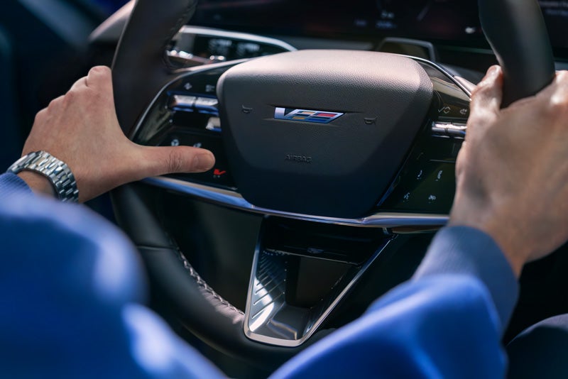 Close-up of a Man About to Press the V-Button on the 2026 OPTIQ-V Steering Wheel | Springfield Cadillac in N. Springfield VT